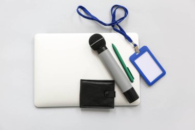 Modern laptop, mikrofon, gri arka planda boş rozet ve cüzdan.