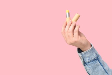 Pembe arka planda dudak kremi olan bir erkek el.