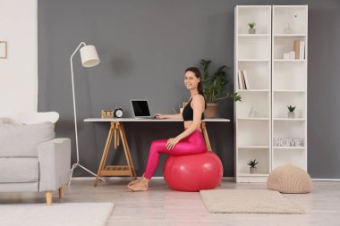 Evde spor yaparken dizüstü bilgisayar kullanan genç bir kadın.