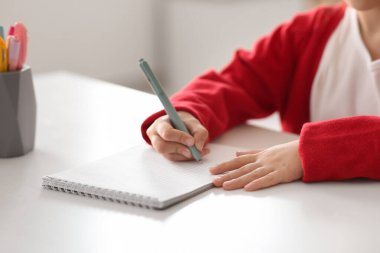 Not defteri ve kalemi olan sevimli küçük bir kız. Masada oturuyor ve evde ders çalışıyor. Yakın plan.