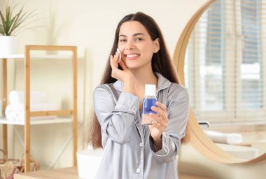 Beautiful young happy woman with cotton pad and bottle of micellar water at home
