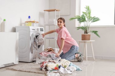 Kirli çamaşırları evdeki çamaşır makinesine koyan genç bir kadın.