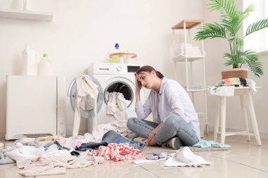 Çamaşır makinesinin yanında kirli çamaşırları olan yorgun genç bir kadın.