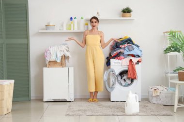 Çamaşır makinesinin üstündeki kirli çamaşırlarla şok olmuş genç bir kadın.