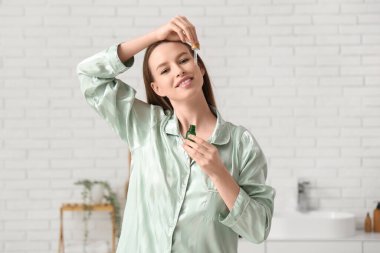 Pijamalı güzel bir kadın banyoda yüzüne kozmetik yağ sürüyor.