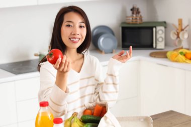 Genç Asyalı kadın mutfaktaki marketten taze ürünleri çıkarıyor.