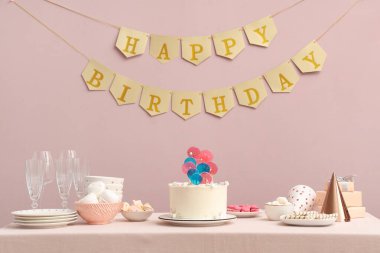 Pasta, şeker ve doğum günü partisi için pembe duvarlı bir masa.