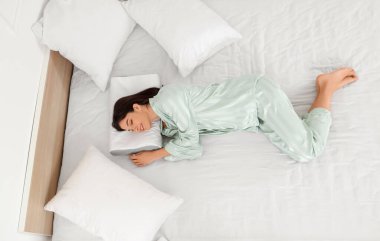 Pijamalı genç bir kadın evdeki rahat ortopedik yastıkta yatıyor.