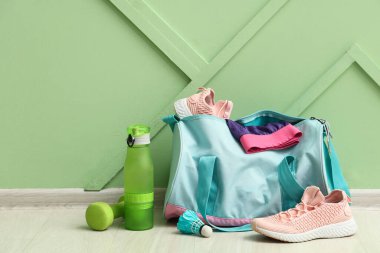 Çantanın içinde farklı spor malzemeleri, spor ayakkabıları ve yeşil duvarın yanında paten.