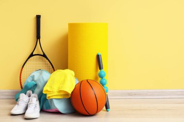 Spor malzemeleri, çanta, paten ve spor ayakkabıları sarı duvarın yanında.