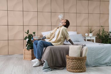 Genç adam tek kullanımlık elektronik sigara içiyor ve evde dinleniyor.