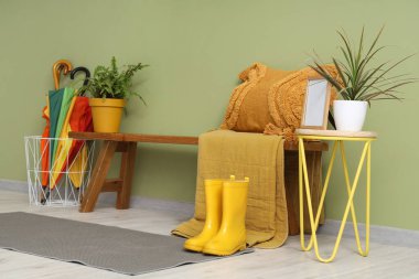 Ahşap bank, sehpa, yastık ve şemsiyeler şık bir odada yeşil duvarın yanında.