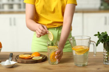 Mutfakta portakallı ve naneli bir bardak limonata tutan genç bir kadın.