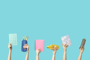 Mavi arka planda kırtasiyeli defter ve kalem kılıfları tutan kadın eller.