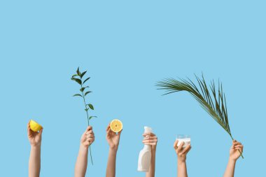 Limon tutan kadın elleri, temizleyici maddeli kavanoz, yeşil dallar ve mavi arka planda bir şişe deterjan.