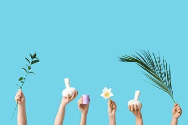 Bitkisel masaj torbaları, çiçek, mum, palmiye yaprağı ve mavi arka planda yeşil dal tutan kadın elleri.