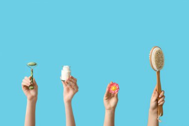 Yüz masajı aletli kadın elleri, şişede deniz tuzu, çiçek ve mavi arka planda masaj vücut fırçası.