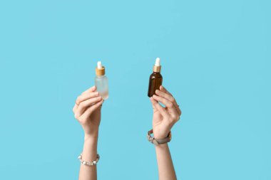 Mavi arka planda kozmetik ürünleri olan kadın elleri