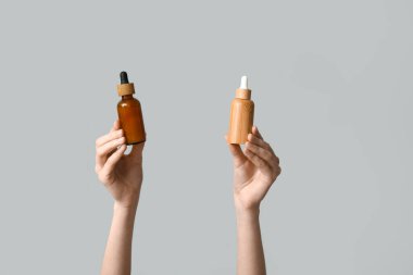 Gri arka planda kozmetik ürünleri şişeleriyle kadın elleri