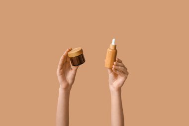 Bej arka planda şişe ve kozmetik ürünlerle dolu kadın elleri