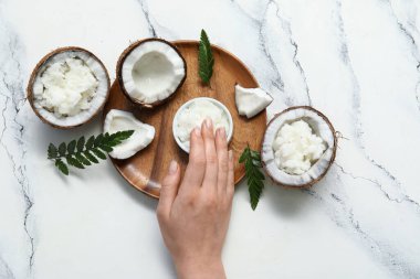 Kadın eli, ahşap tepsi ve mermer arka planda doğal hindistan cevizi yağlı kase.