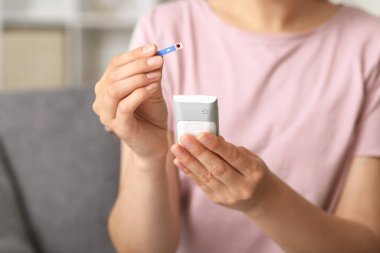 Glikoz testi bandı ve glukometresi olan diyabetik genç kadın evde, yakın plan.