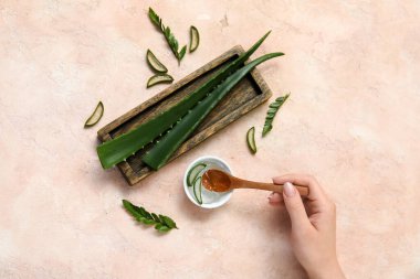 Kaşık ve bej arka planda bir kase aloe vera jeli bir kadın eli.