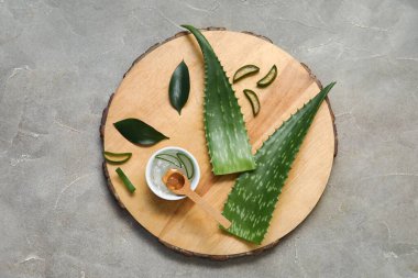 Bir kase aloe vera jeli ve gri arka planda yaprakları olan ahşap tahta.