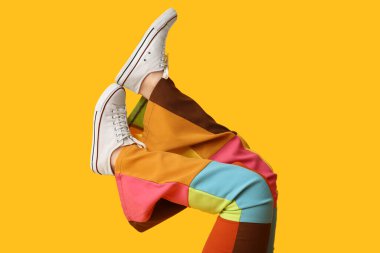 Sarı arka planda şık beyaz ayakkabılı genç kadın bacakları.