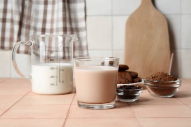 Bir bardak çikolatalı süt ve bej fayans masasında kakao tozu.