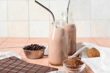 Bir şişe çikolata sütü ve bej döşeme masasında kakao tozu olan cam kase.