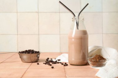 Bir şişe çikolatalı süt ve bej fayans masasında kakao tozu bulunan cam kase.