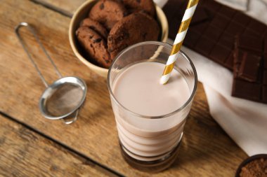 Bir bardak çikolatalı süt ve ahşap arka planda lezzetli kurabiyeler.