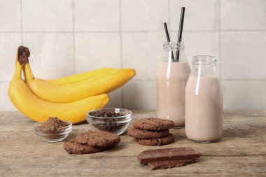 Lezzetli kurabiyeli çikolata sütü şişeleri ve ahşap masada bir kase kakao tozu.