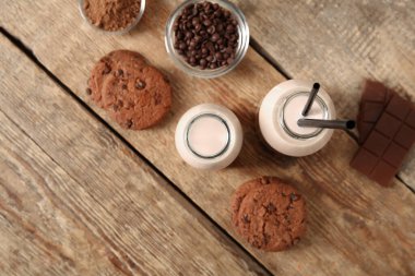 Lezzetli kurabiyelerle dolu bir şişe çikolata sütü ve ahşap zemin üzerinde bir kase kakao tozu.