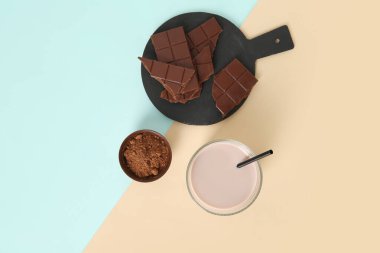 Renkli arka planda kakao tozuyla bir bardak çikolatalı süt ve kase.