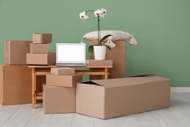 Boş dizüstü bilgisayar, taşınan kutular ve yeşil duvarın yanında orkide çiçeği.