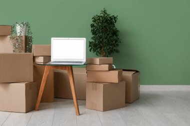 Boş dizüstü bilgisayar, yeşil duvarın yanındaki kutuların ve bitkilerin taşındığı masada.