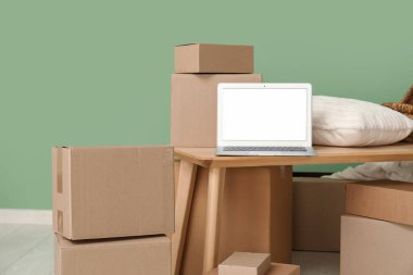 Masada yastık ve yeşil duvarın yanındaki kutuları taşıyan boş bir laptop.