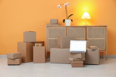 Boş dizüstü bilgisayar, taşınan kutular ve turuncu duvarın yanında tuvalet.