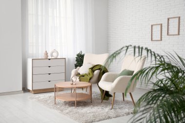 Koltuklar, yastıklar, ekose, sehpa ve çekmeceler odada.