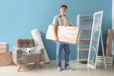 Genç adam evinde streç sarılı bir masa taşıyor.