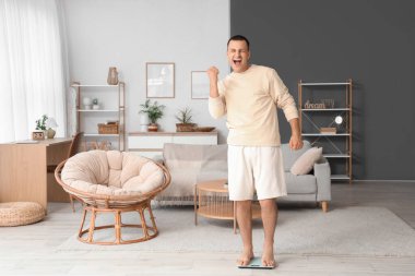 Mutlu genç adam ağırlığını evde tartıyla ölçüyor.