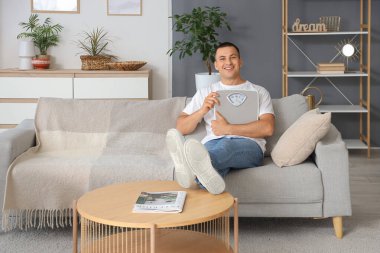 Ağırlık tartısı olan genç adam evdeki kanepede oturuyor.