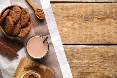 Bir bardak çikolatalı süt ve ahşap arka planda lezzetli kurabiyeler.