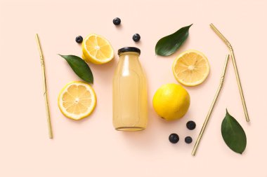 Dilimlenmiş limon, pipet, böğürtlen ve soluk pembe arka planda bir şişe kombu çayı.