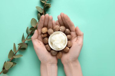 Turkuaz arka planda tereyağlı ve fındıklı kaseyi tutan kadın eller.