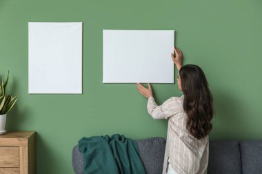 Genç ve güzel bir kadın oturma odasındaki yeşil duvara resim asıyor.