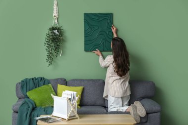 Genç ve güzel bir kadın evdeki yeşil duvara resim asıyor.