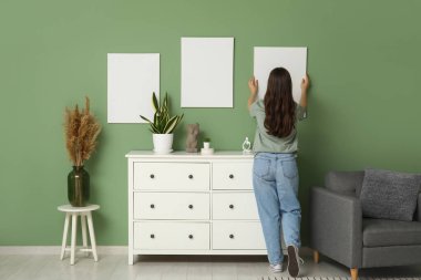 Evdeki yeşil duvara boş tuval asan genç bir kadın. Arka plan